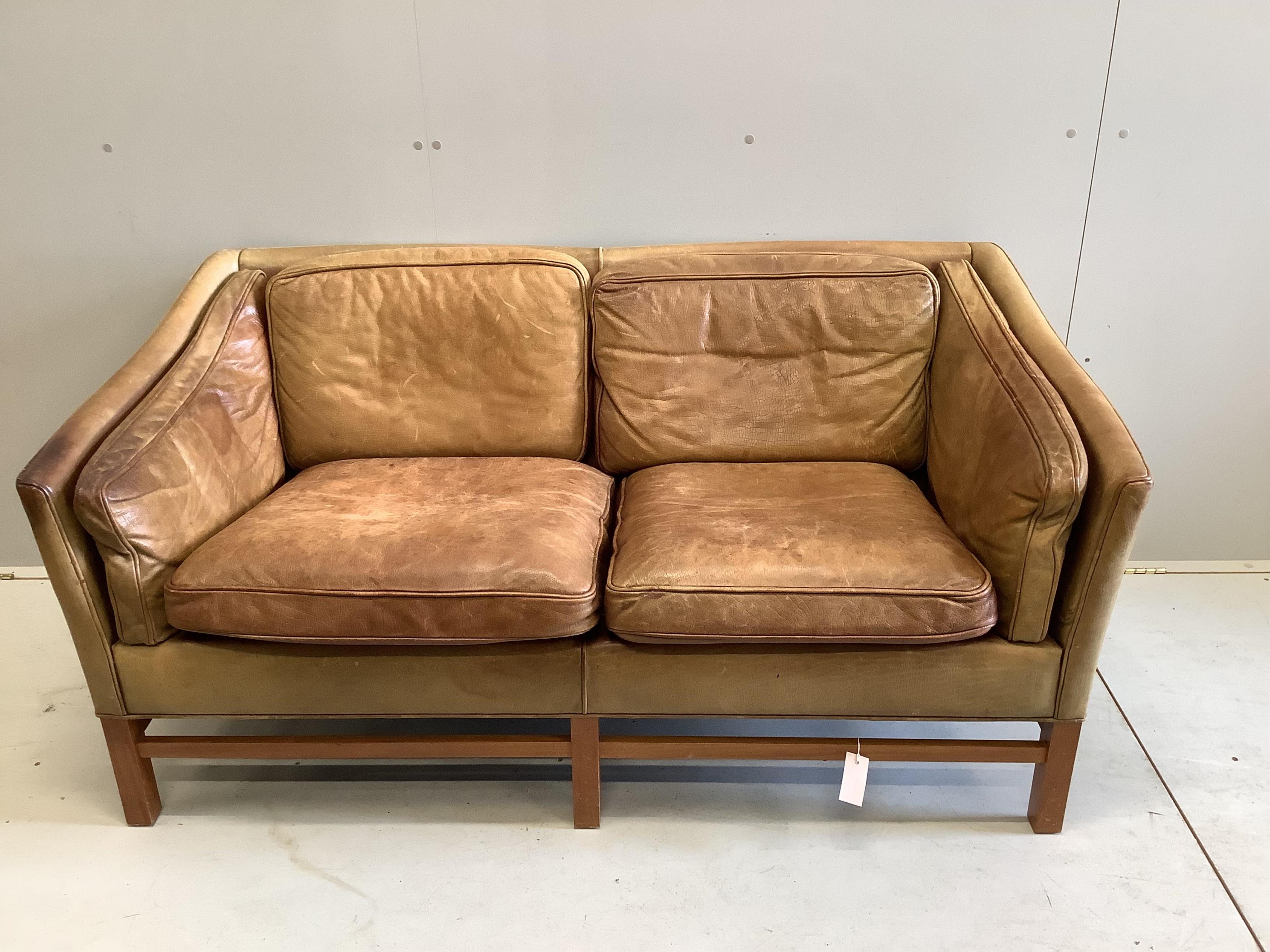 A mid century Danish teak and faded tan leather upholstered two seater settee, width 153cm. Condition - heavily faded from a light burgundy tone now down to pale tan